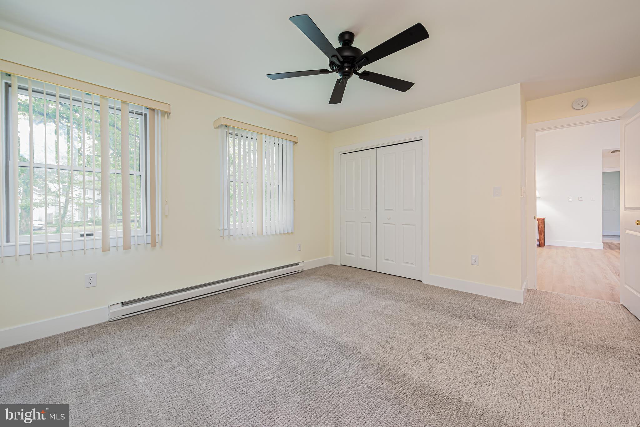 Empty carpeted bedroom with two windows, a ceiling fan, and a double-door closet.