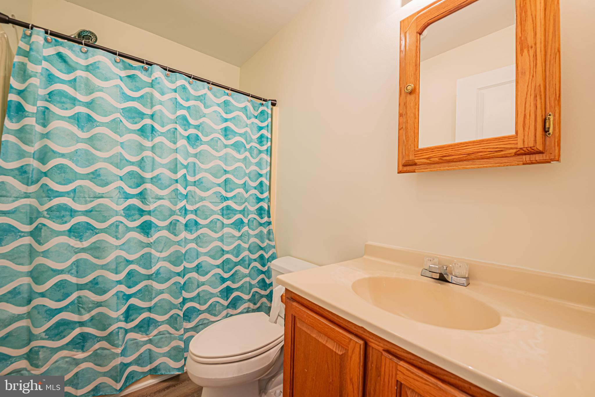 Bathroom with a turquoise wavy shower curtain and a wood vanity with a cream sink.