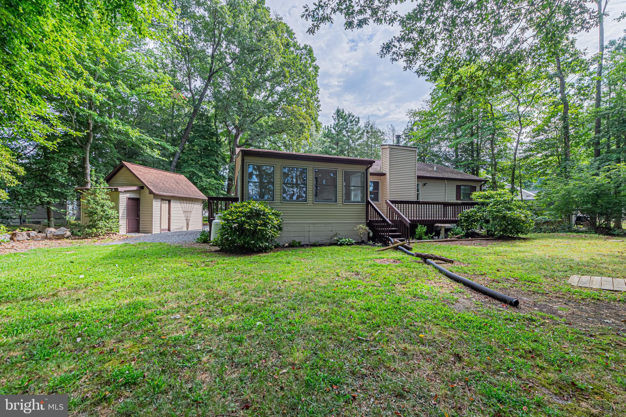 Rear of a single-story home with a raised deck, detached outbuilding, and wooded lawn.