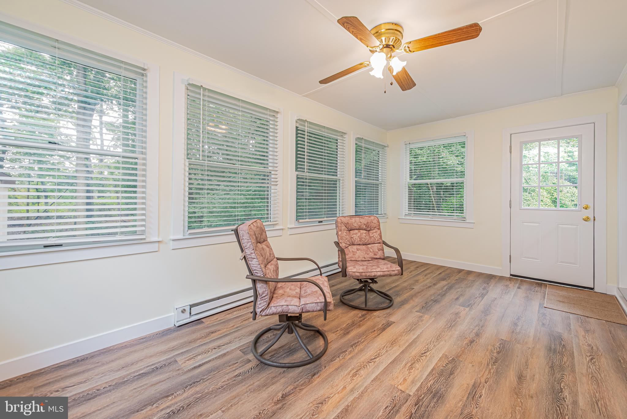 Sunroom with two cushioned swivel chairs, wood-look flooring, and windows along the wall.