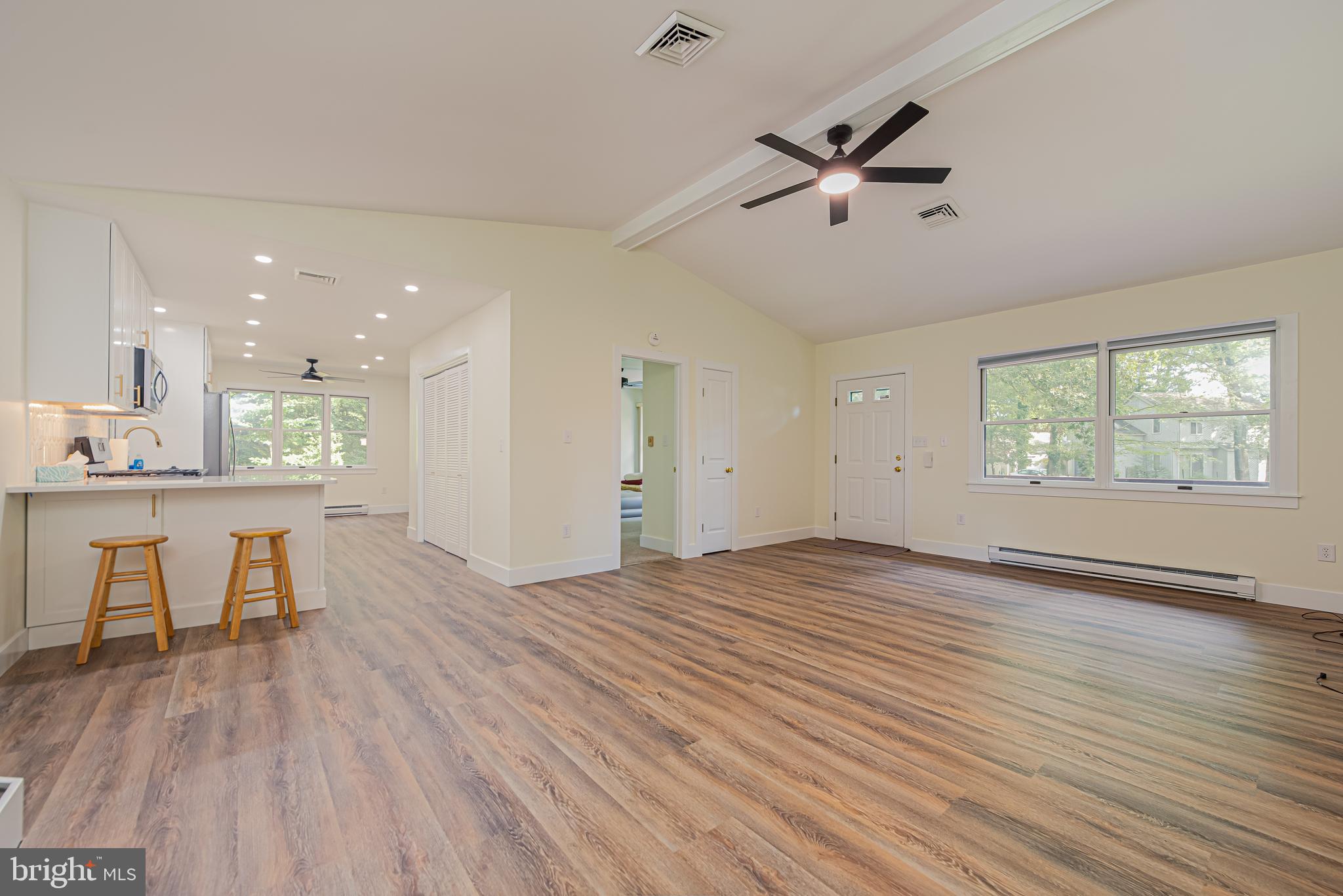 Open living area with wood-look floors, a kitchen breakfast bar, and large windows.