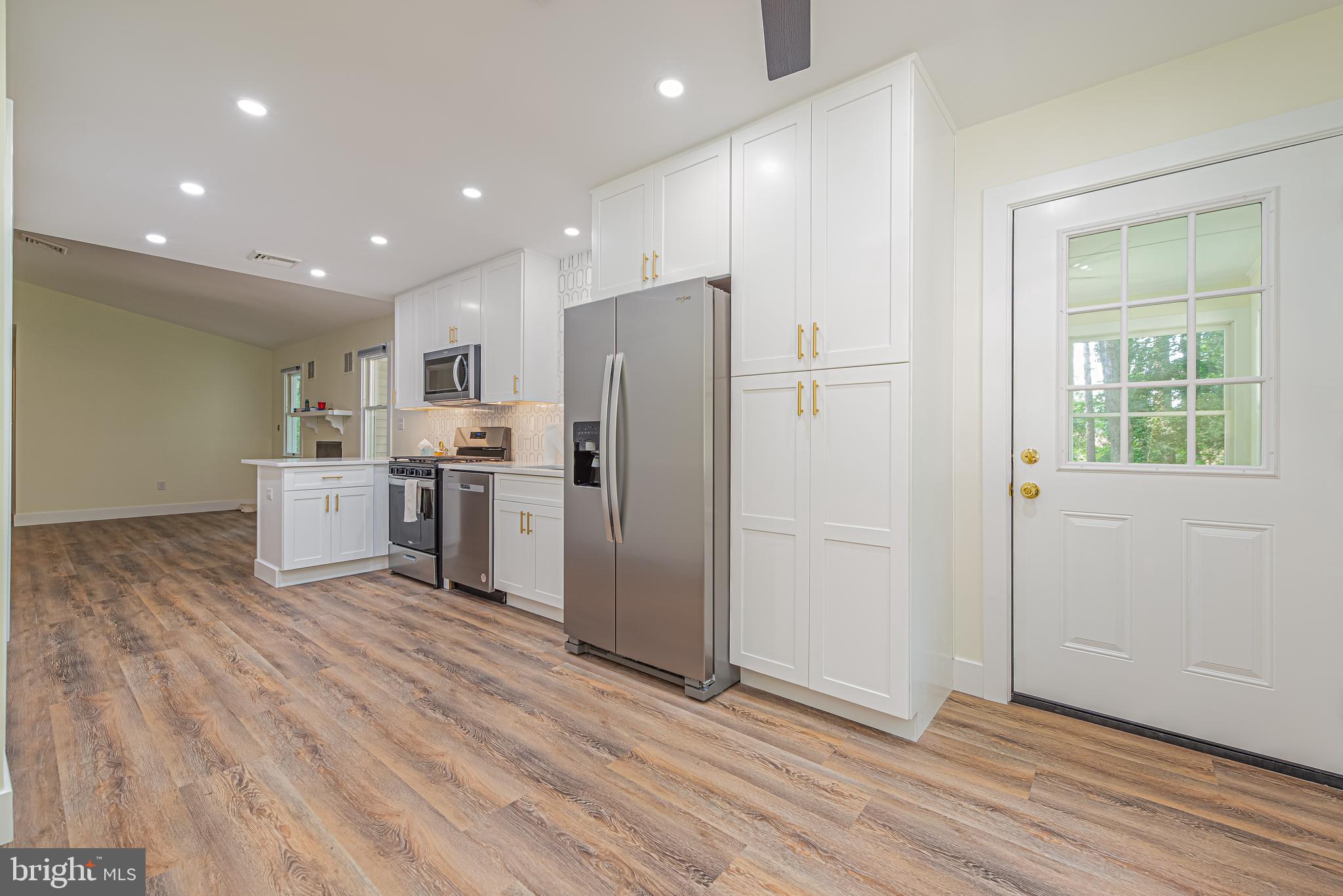 Open kitchen with white cabinets, stainless steel appliances, gold-tone hardware, and wood-look flooring.