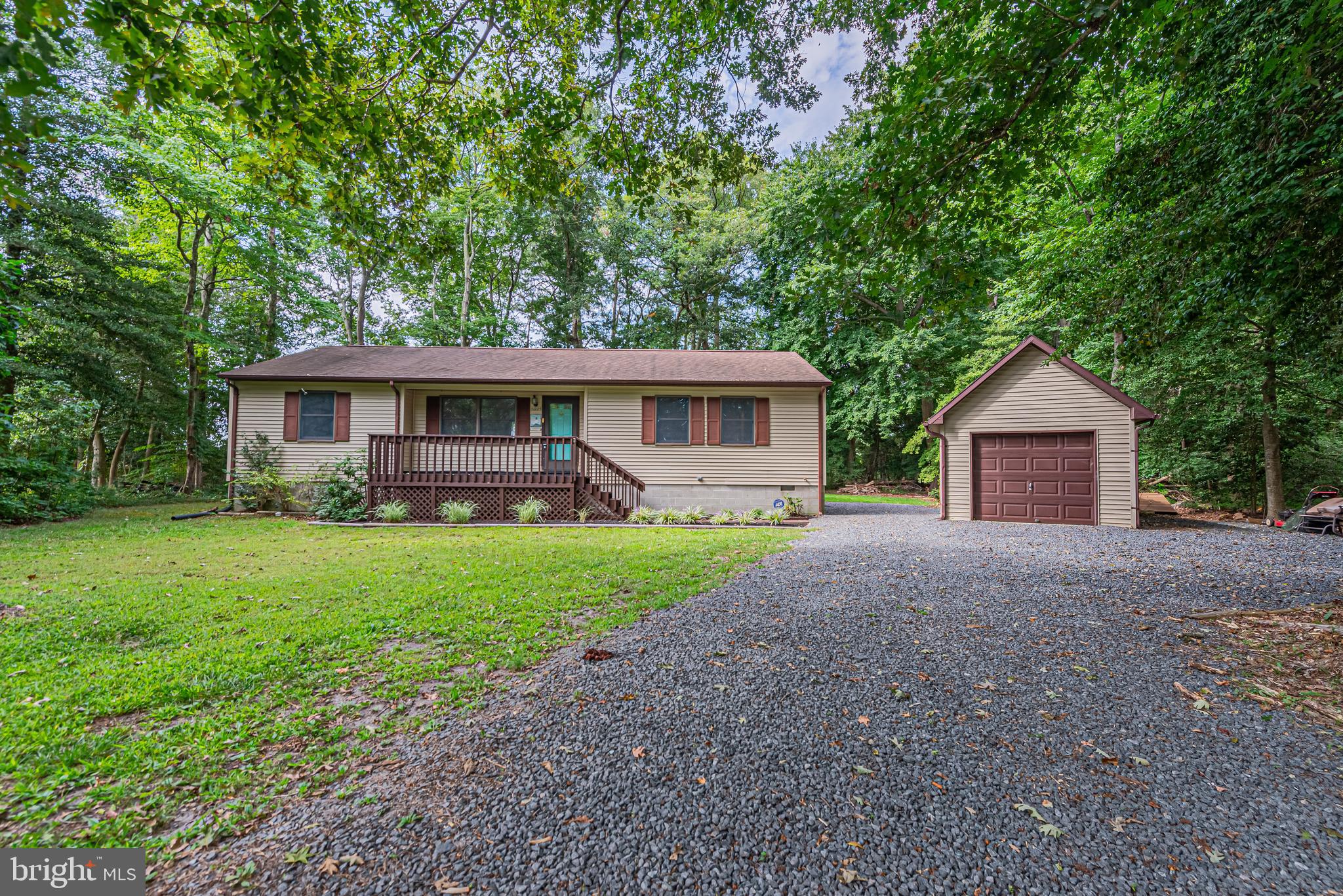 Single-story home with a raised front porch, detached garage, and gravel driveway amid trees.