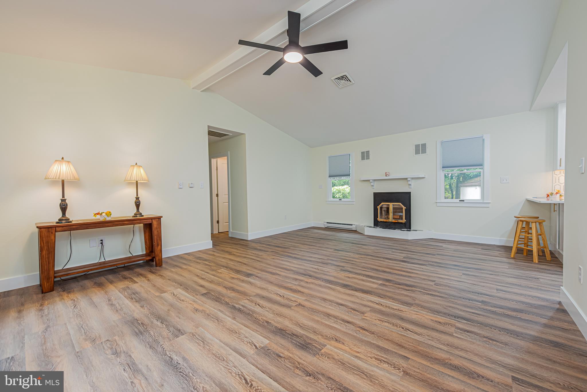 Open living room with vaulted ceiling, wood-look floors, and a fireplace between two windows.