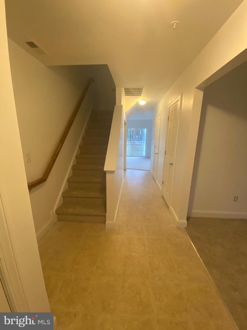 Hallway with a carpeted staircase, wooden handrail, and glass door at the far end.