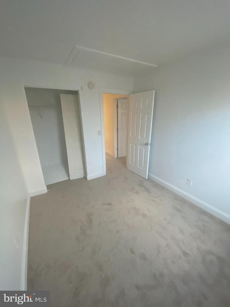 Empty carpeted bedroom with an open closet and doorway to a lit hallway.