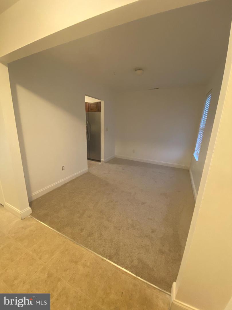 Empty carpeted room with a window and an opening to the kitchen.