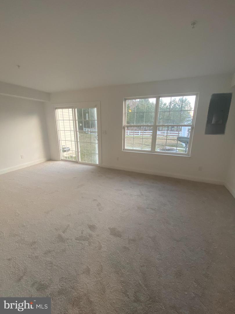Empty carpeted living room with a sliding glass door and large window overlooking a fenced yard.