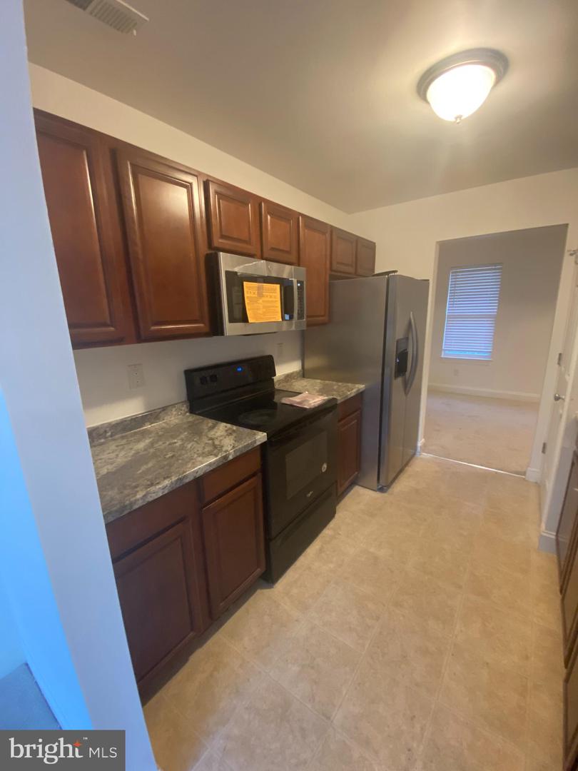 Kitchen with dark wood cabinets, stone-look counters, stainless steel appliances, and a black range.
