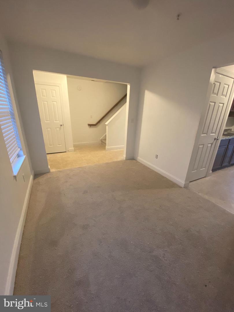 Unfurnished carpeted room with a window, stairway opening, and doorway beside kitchen cabinets.