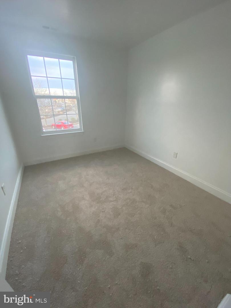 Empty bedroom with beige carpet and a tall window overlooking a red car.