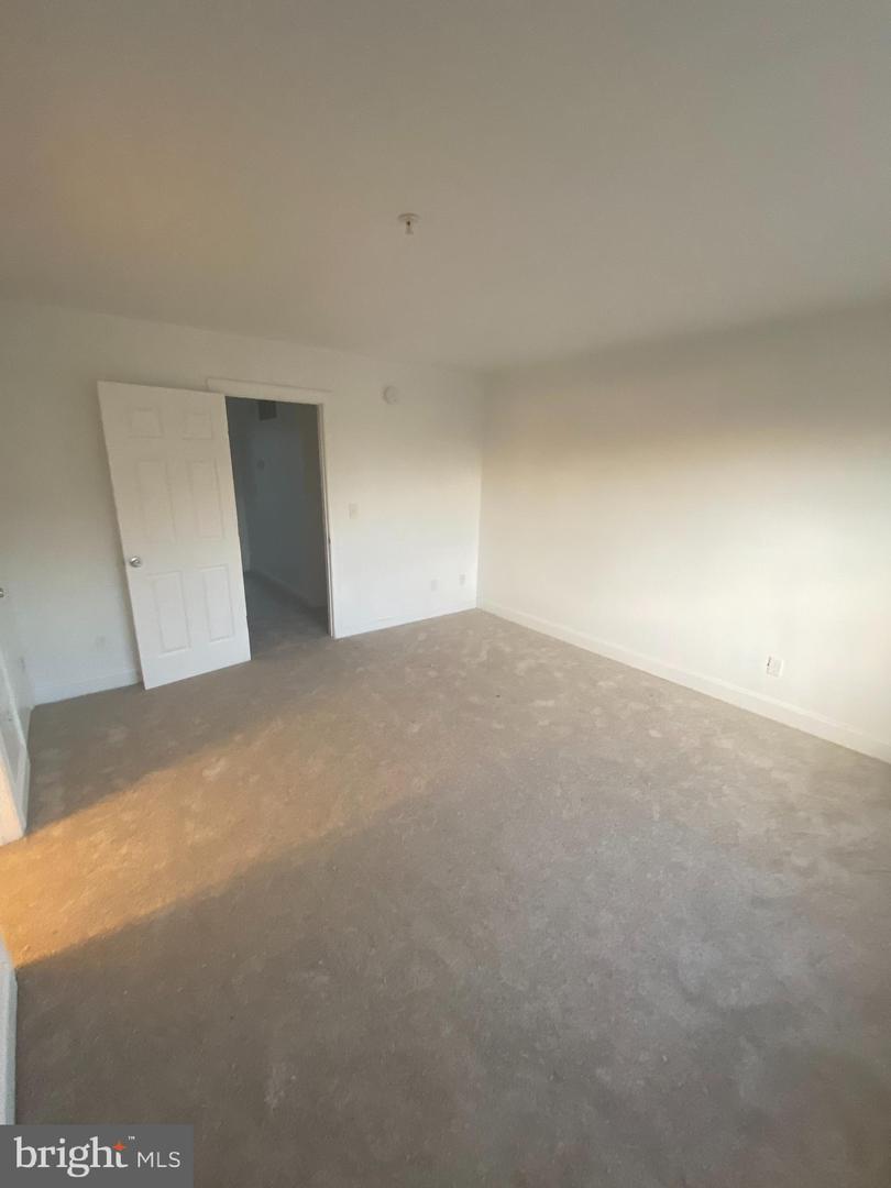 Vacant carpeted room with white walls and an open door to a hallway.
