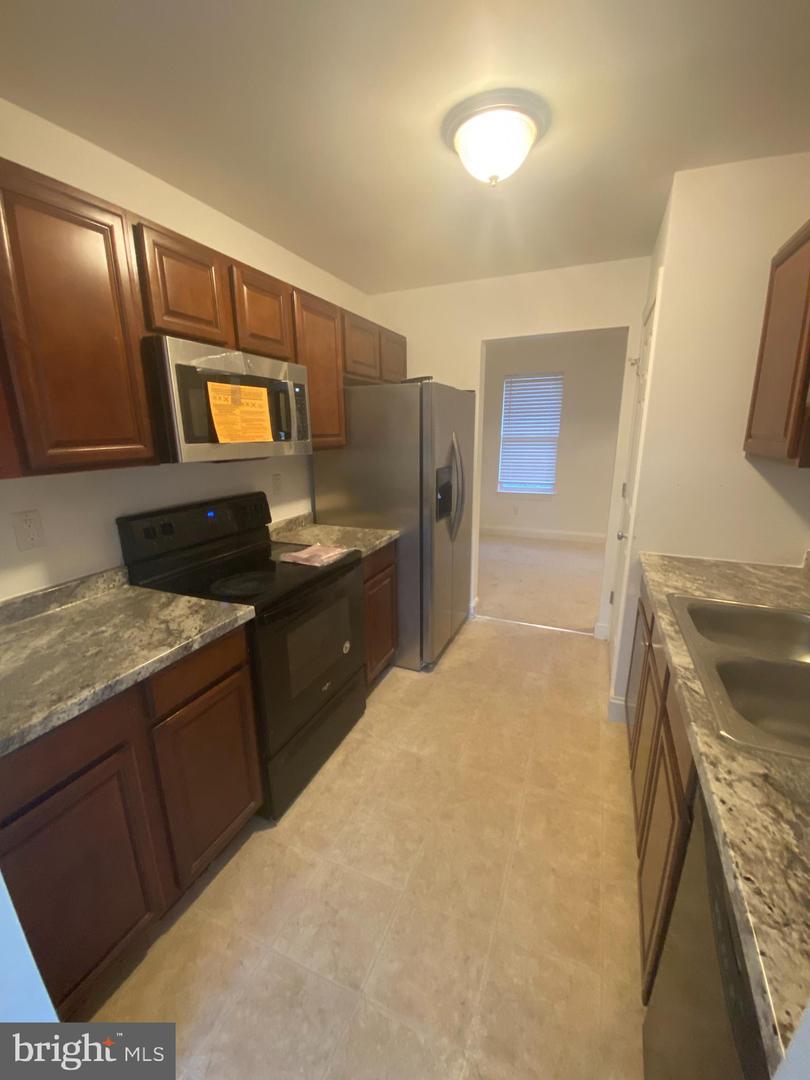 Galley kitchen with dark wood cabinets, patterned countertops, and stainless steel appliances.