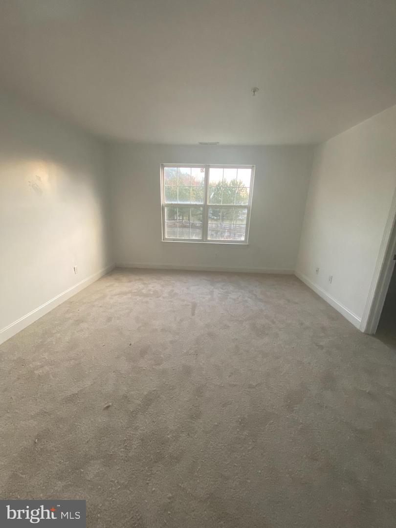 Empty carpeted room with white walls and a four-pane window overlooking trees and water.