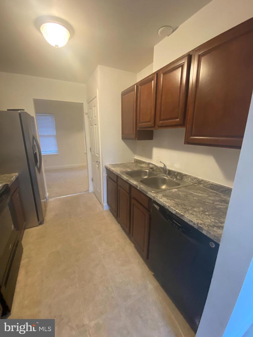 Kitchen with dark wood cabinets, stone counters, double sink, and stainless steel refrigerator.