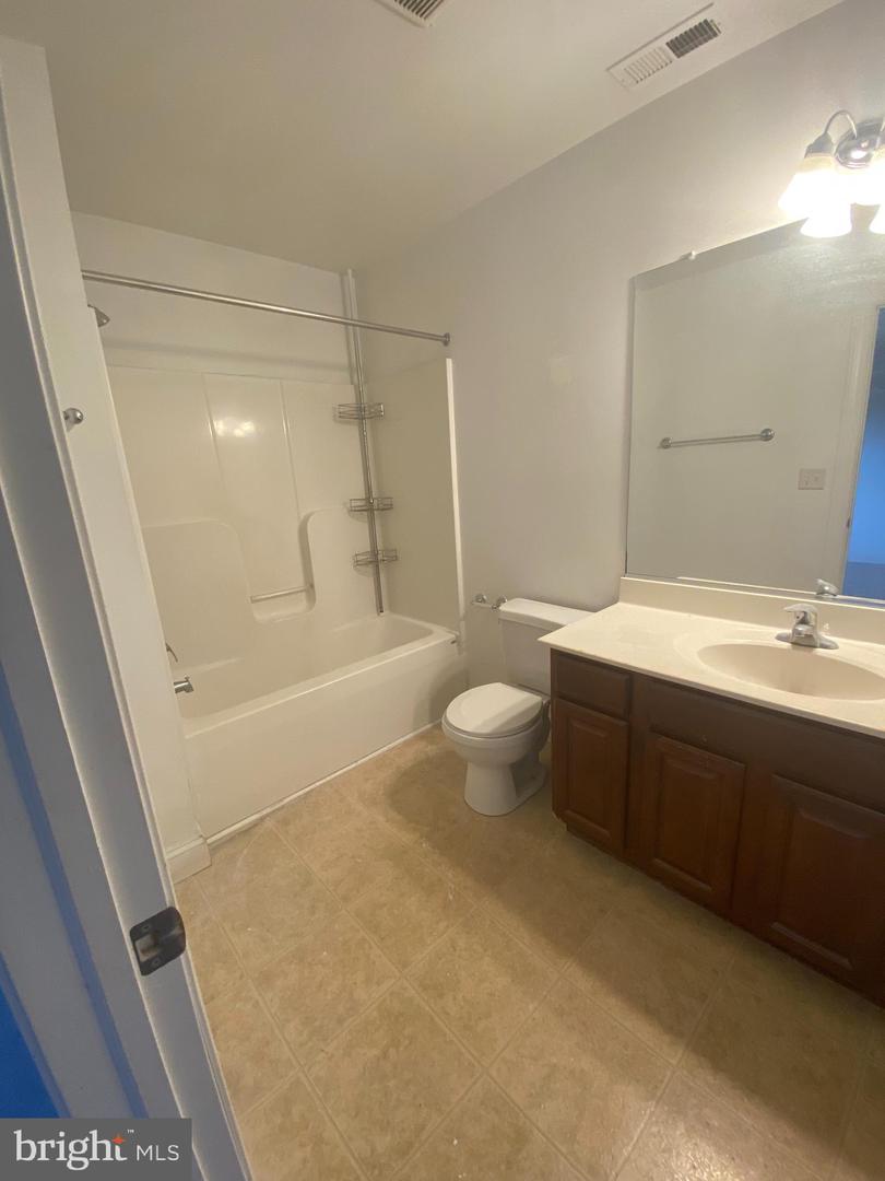 Bathroom with a tub-shower, toilet, and dark wood vanity with a large mirror.