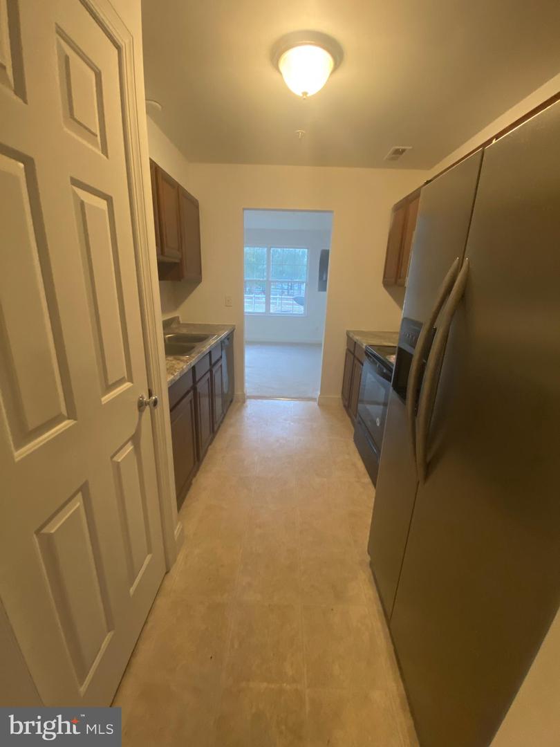 Galley kitchen with dark cabinets, stainless steel appliances, and a doorway to a bright room.