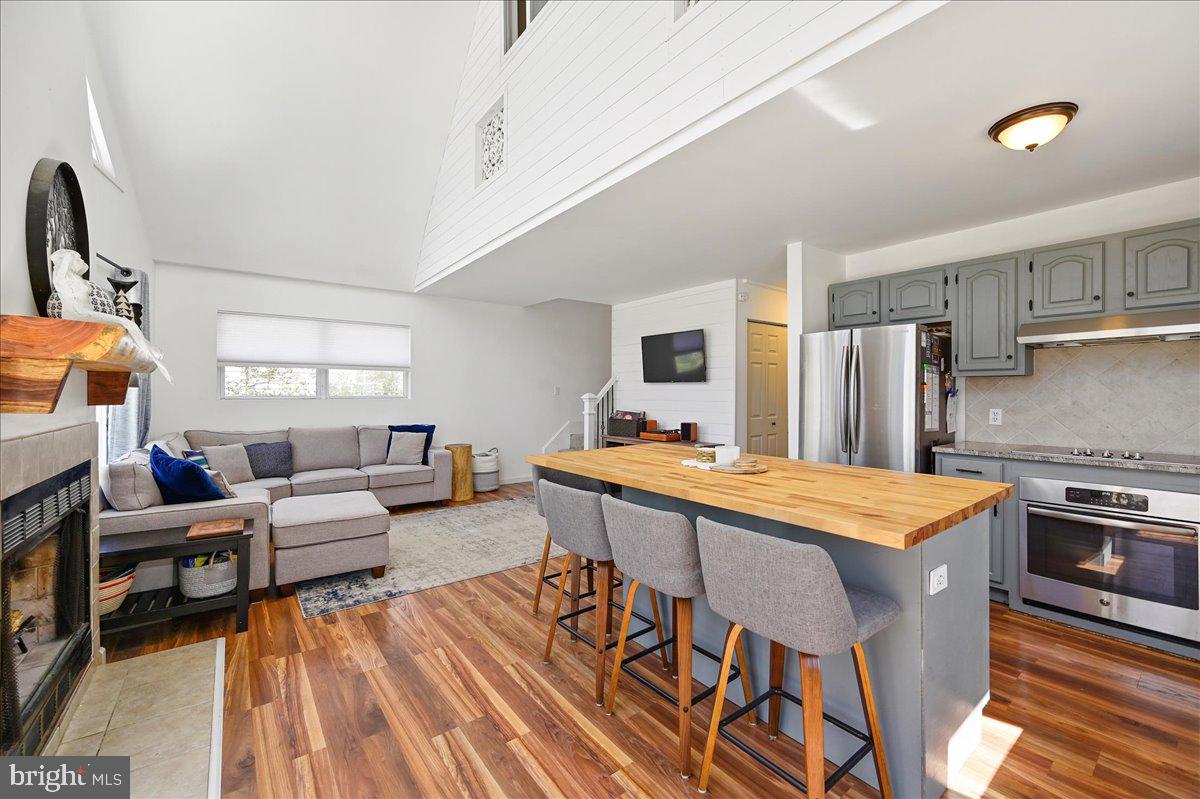 Open living room and kitchen with vaulted ceiling, fireplace, gray sectional, and oversized island.