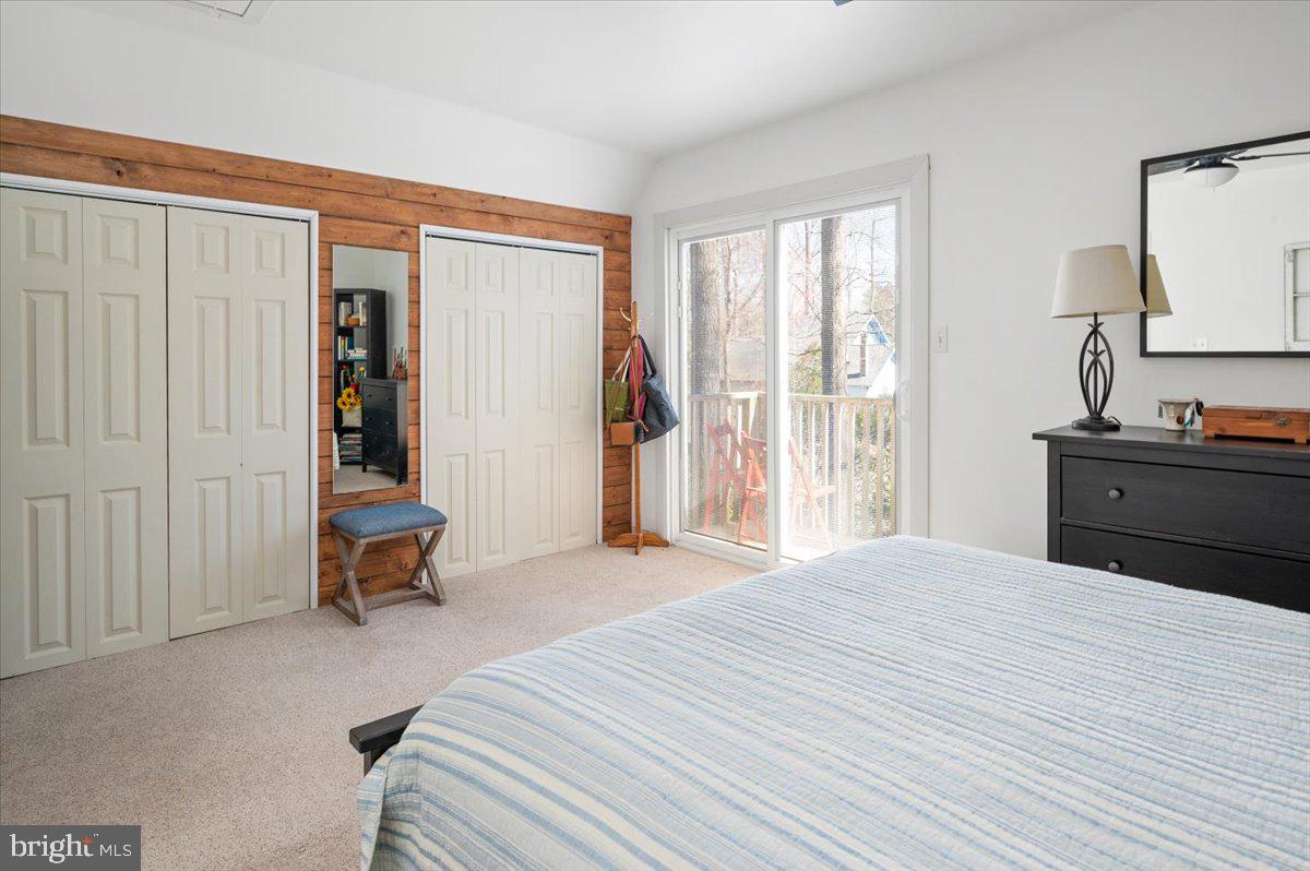 Bedroom with a striped bedspread, wood-paneled accent wall, and sliding glass doors to a deck.