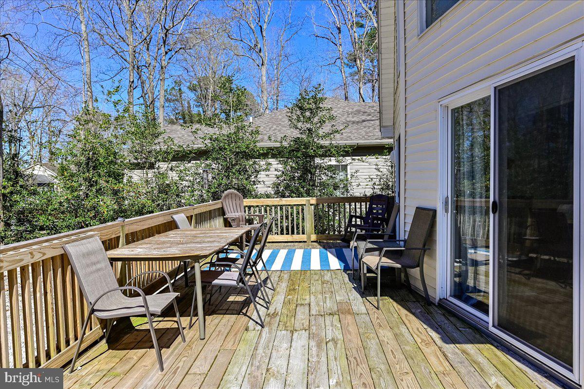 Wooden deck with outdoor dining set, lounge chairs, and a striped rug beside sliding glass doors.