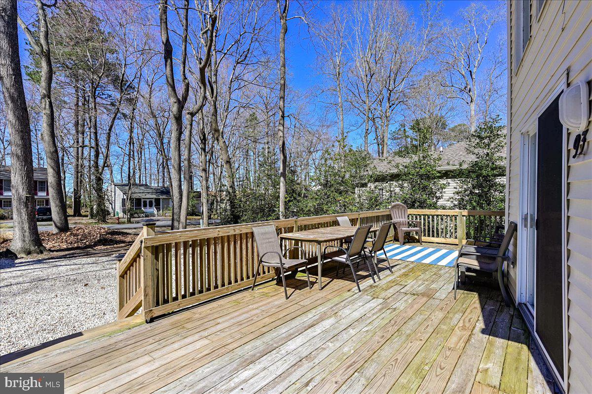 Wooden deck with outdoor dining set, lounge chairs, and a blue-and-white striped rug.