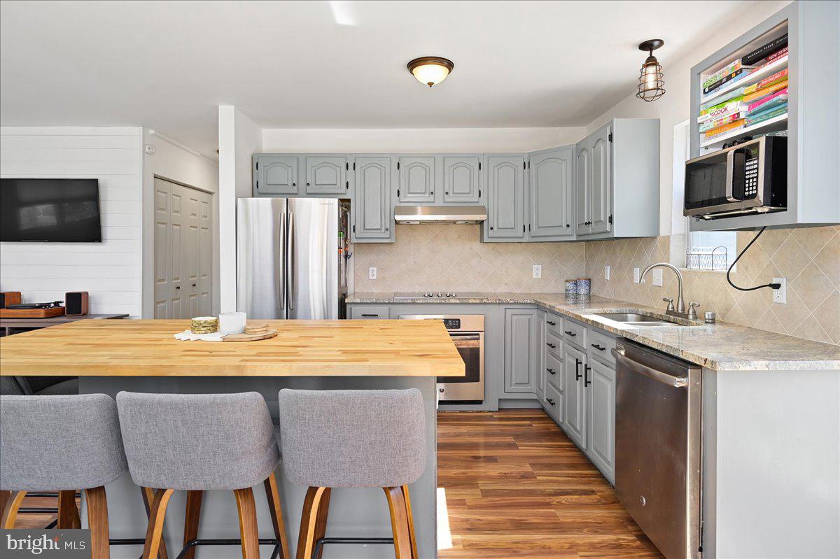 Kitchen with gray cabinets, stainless appliances, and a butcher-block island with three stools.