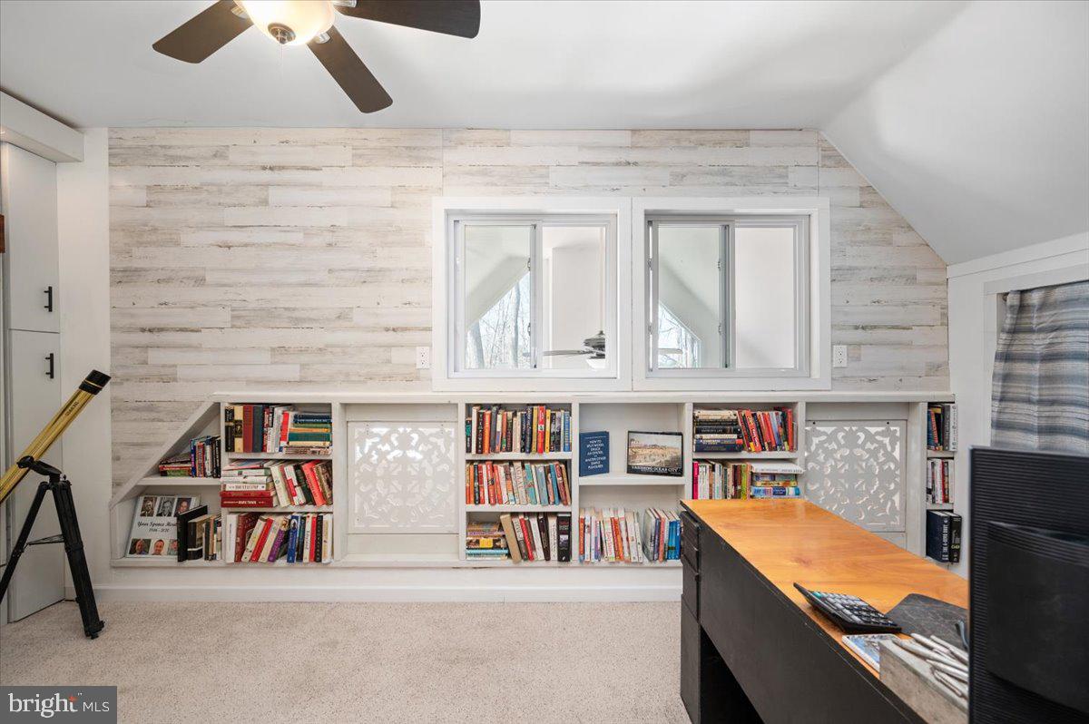 Home office with built-in bookshelves, two windows, and a desk beneath a sloped ceiling.