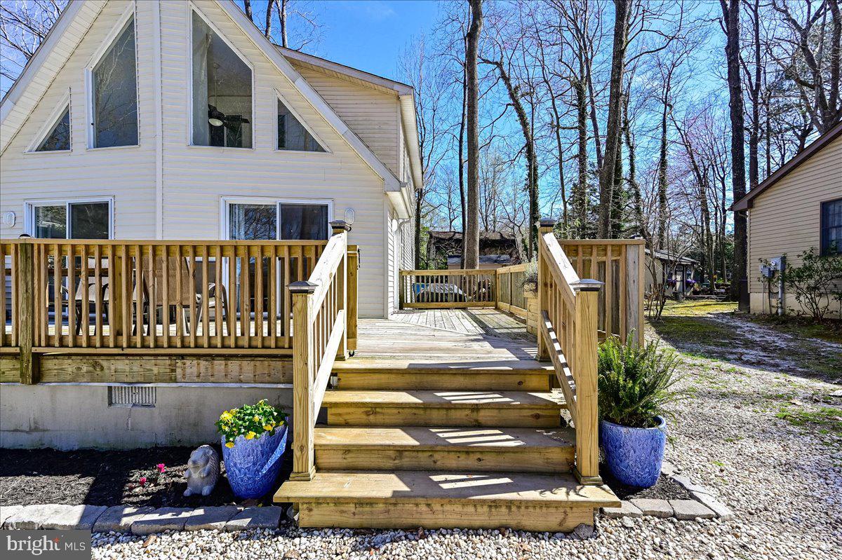 Light-sided home with a broad wooden deck, central stairs, and blue flower planters.