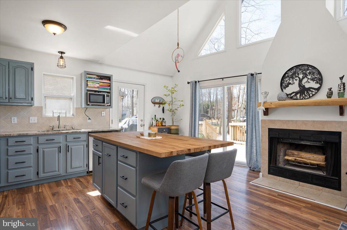 Open kitchen with a wood-topped island, blue-gray cabinets, and a fireplace beside sliding doors to a deck.