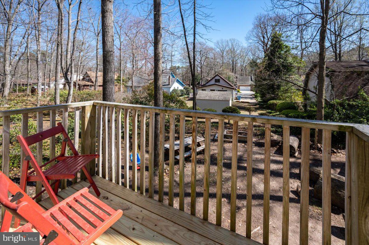 Wooden deck with red Adirondack chairs overlooking a wooded yard and nearby homes.