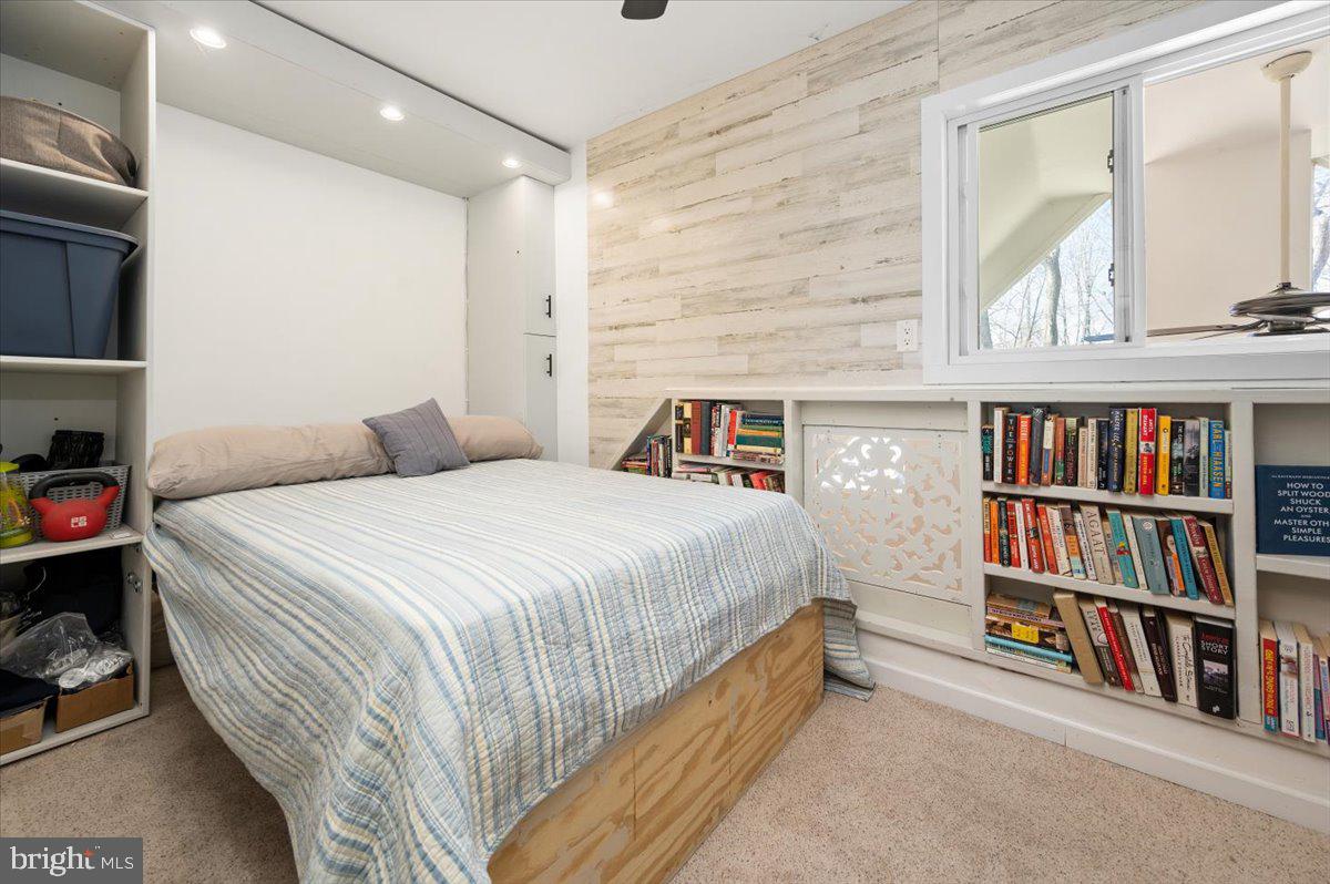 Bedroom with striped bedding, built-in bookshelves, and a pale wood-look accent wall.