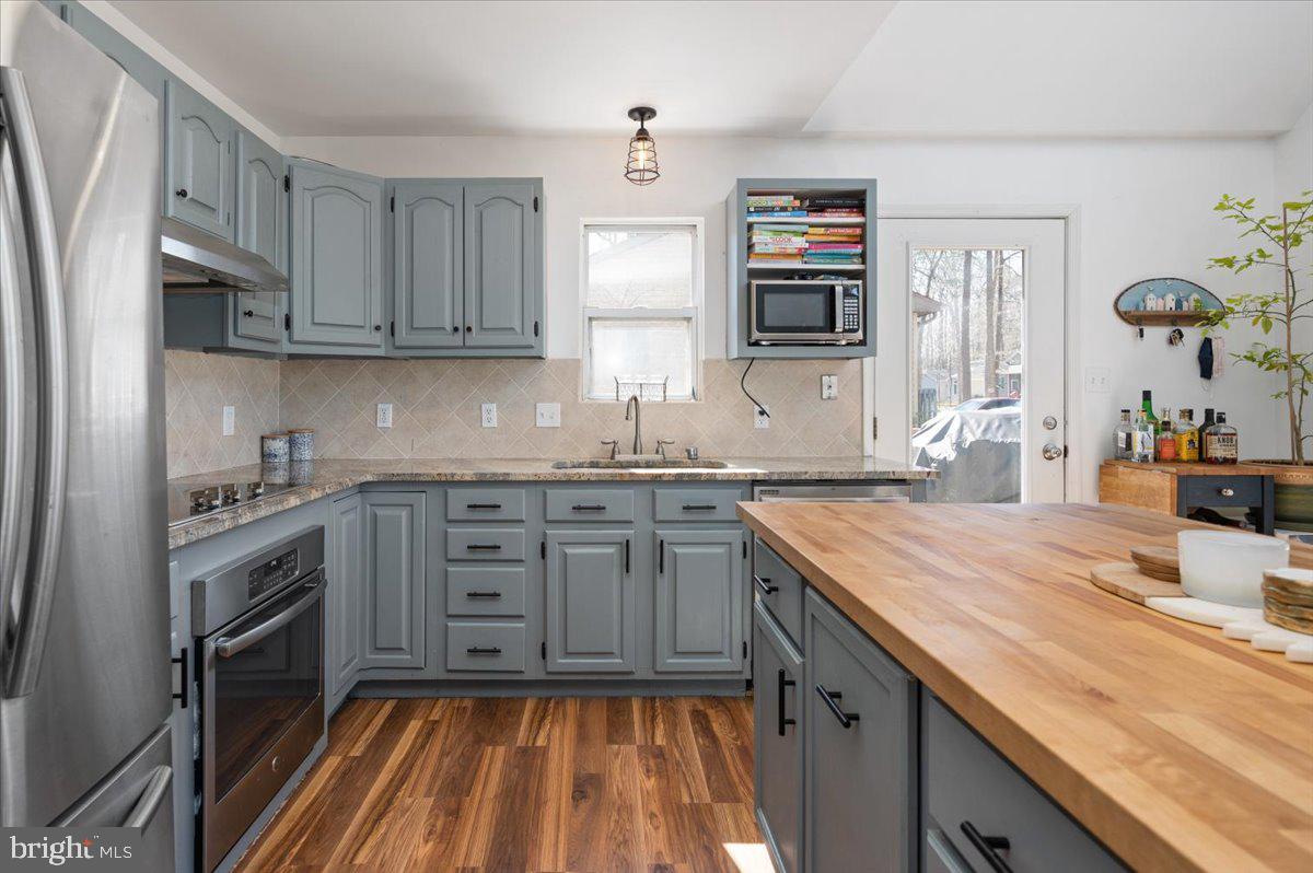Kitchen with gray cabinets, stainless appliances, a large butcher-block island, and warm wood floors.
