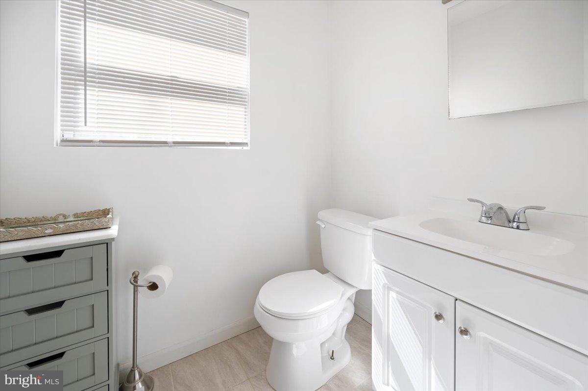 Bathroom with a white toilet, sink vanity, gray cabinet, and window blinds.