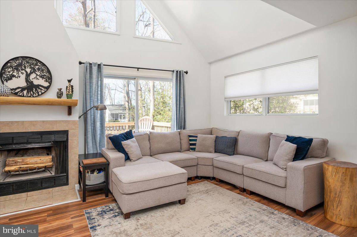 Living room with a vaulted ceiling, beige sectional, tiled fireplace, and windows overlooking a deck.
