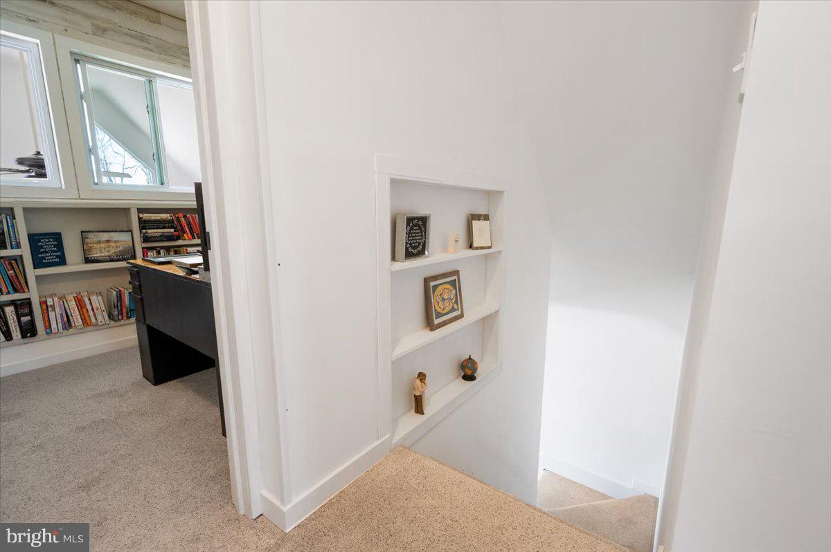 Carpeted stair landing with a built-in display shelf beside a book-lined office.