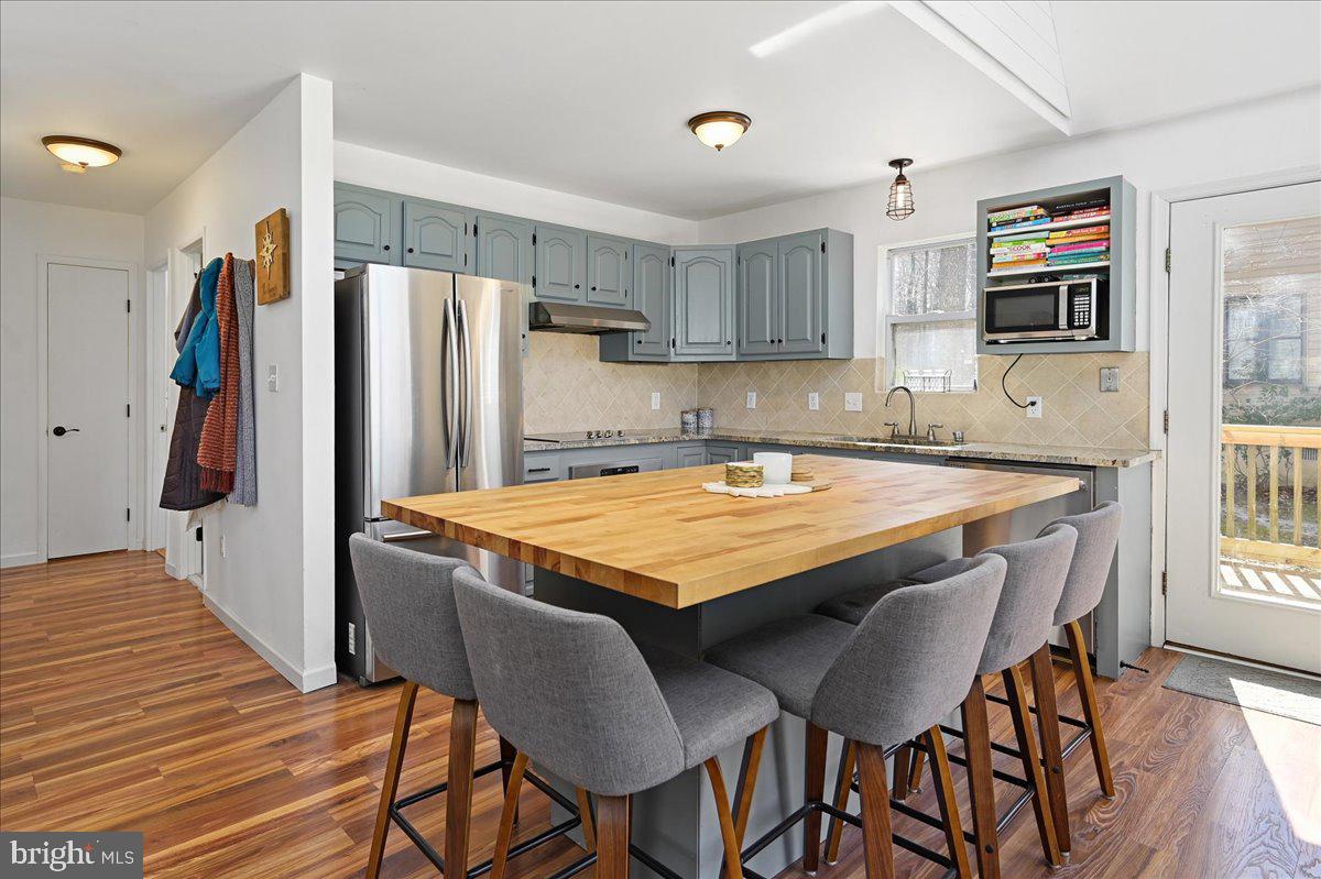 Kitchen with blue-gray cabinets, stainless appliances, and a large butcher-block island with gray stools.