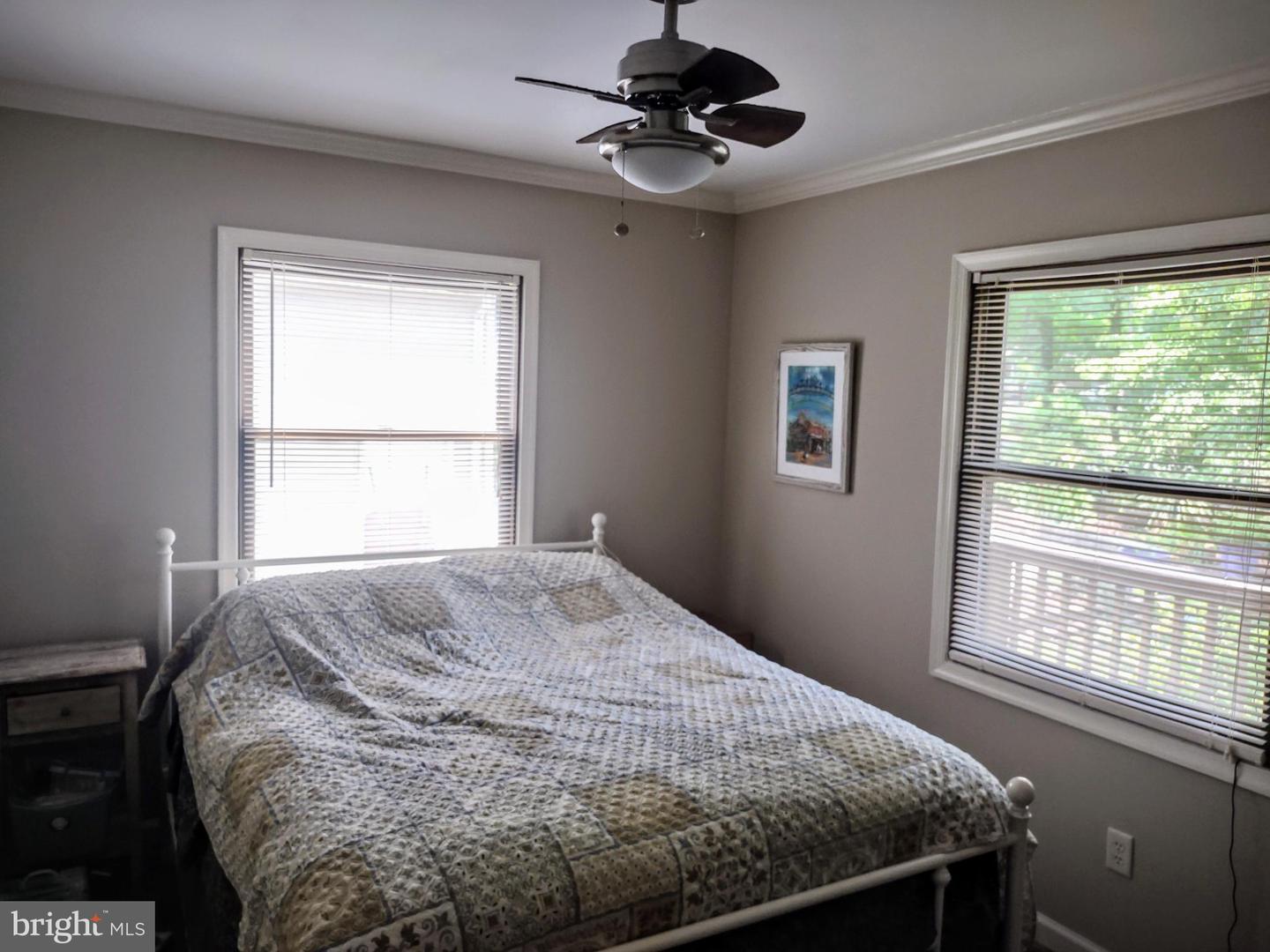Bedroom with a patterned quilt on a white metal bed and two windows with blinds.