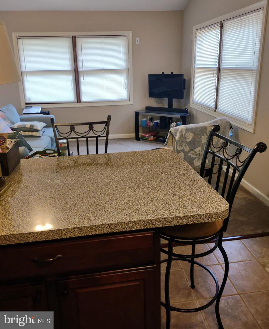 Kitchen with a large speckled granite peninsula and black metal bar stools beside a carpeted living area.