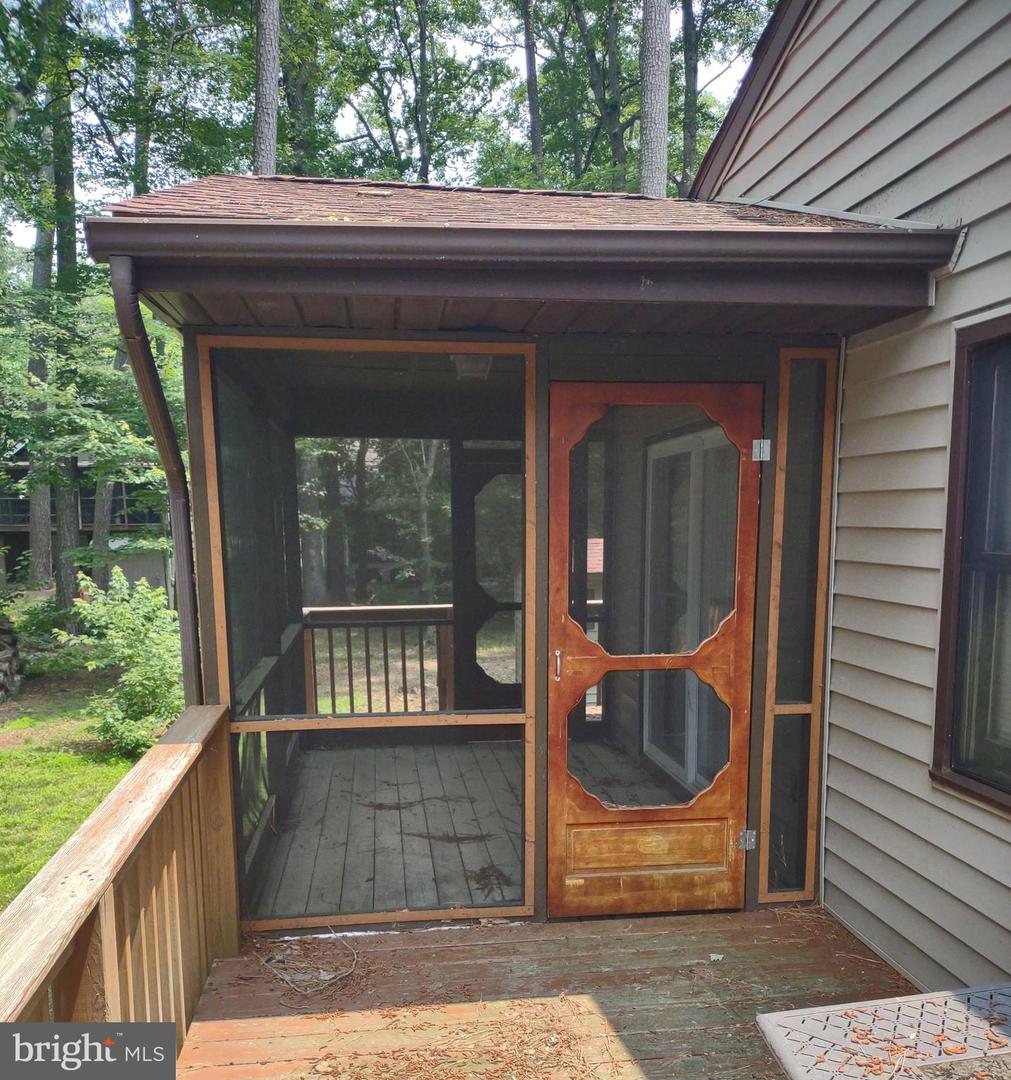 Screened porch with a wooden door and deck railing beside a wooded yard.