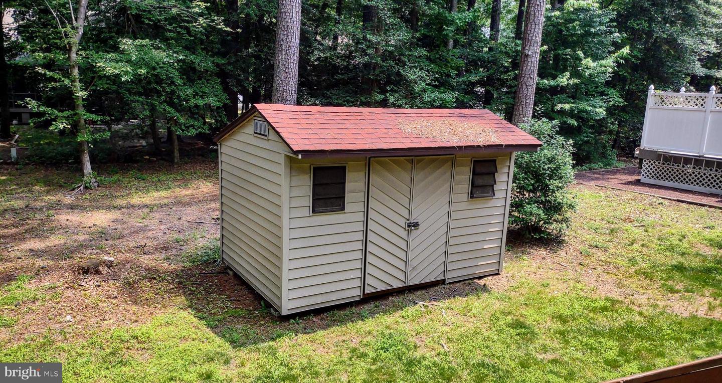 Beige backyard shed with a red roof, double doors, and windows among trees.