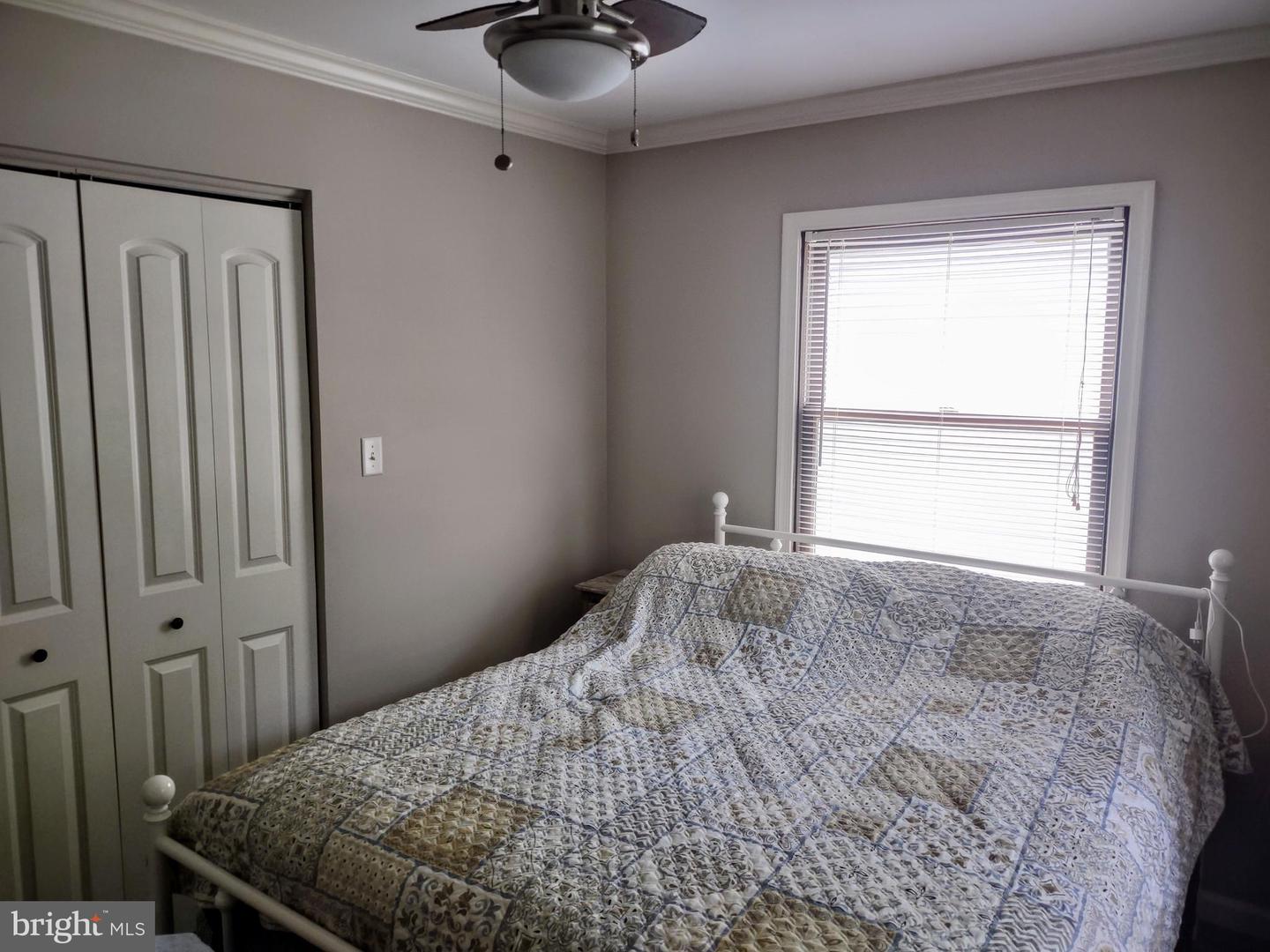 Bedroom with a patterned quilt on a white metal bed, paneled closet doors, and a window with blinds.