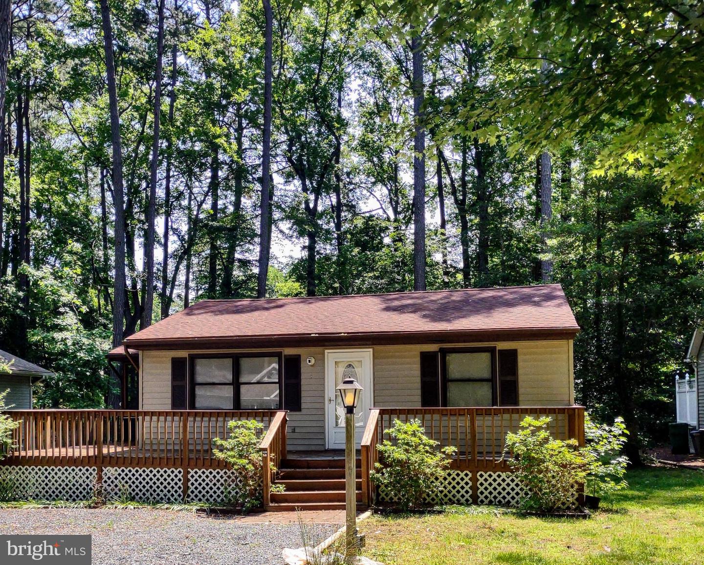 Single-story home with a wooden front deck and steps, set among mature trees.
