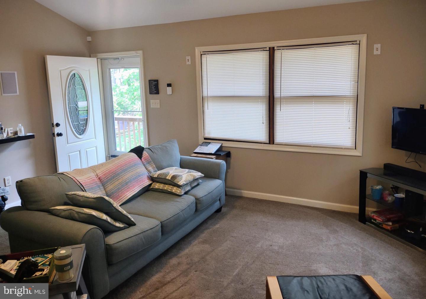 Living room with a gray sectional, beige carpet, and a large window with blinds.