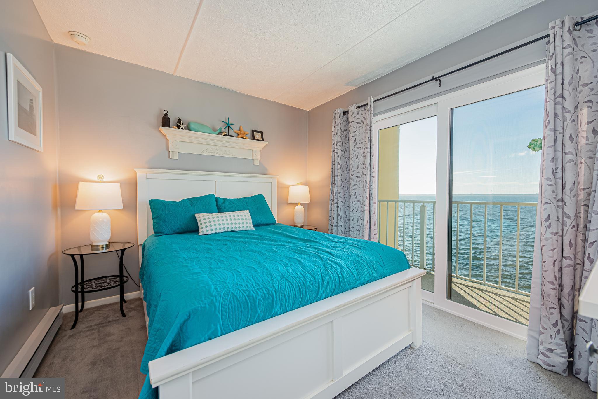 Furnished bedroom with a turquoise bedspread and sliding doors overlooking the water.