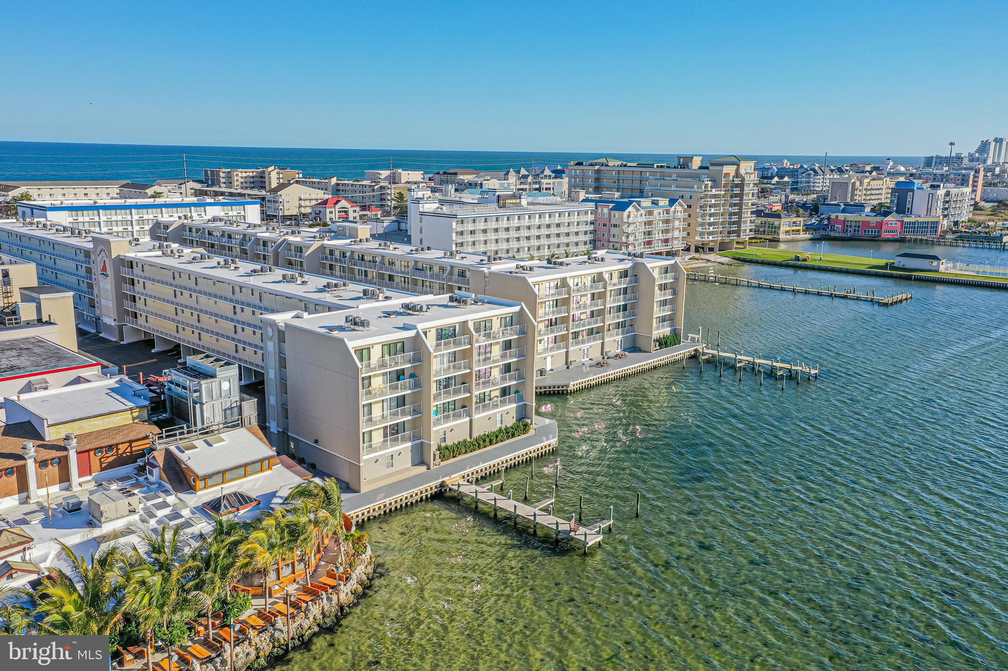 Aerial view of waterfront condominium buildings beside the bay, with the ocean on the horizon.