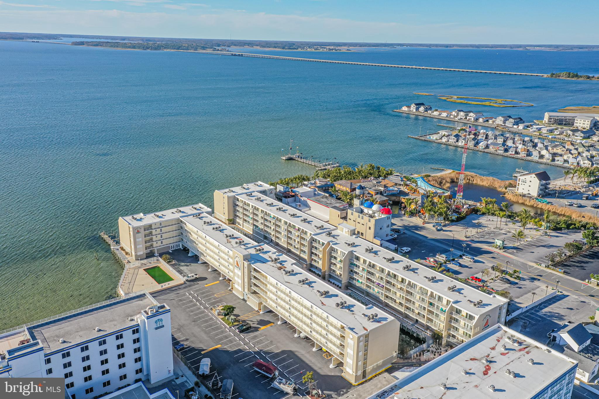 Waterfront condominium complex with long rows of balconies beside a broad bay and distant bridge.