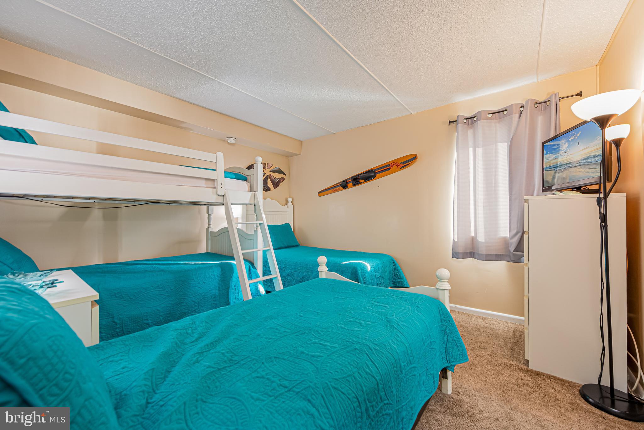 Bedroom with teal-covered beds, a white bunk bed, and surfboard wall decor