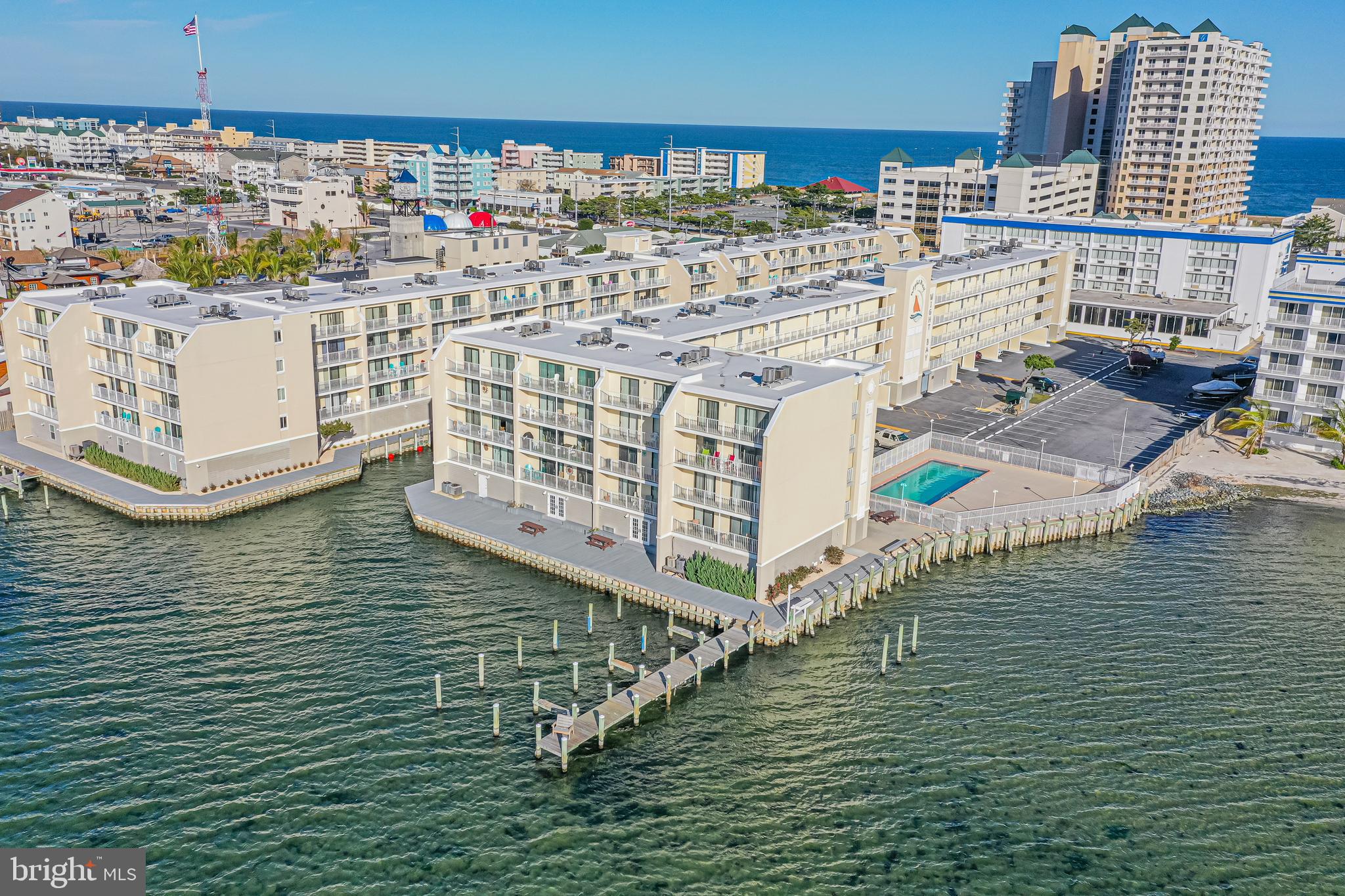 Waterfront condominium complex with dock, pool, and ocean beyond, photographed from above.