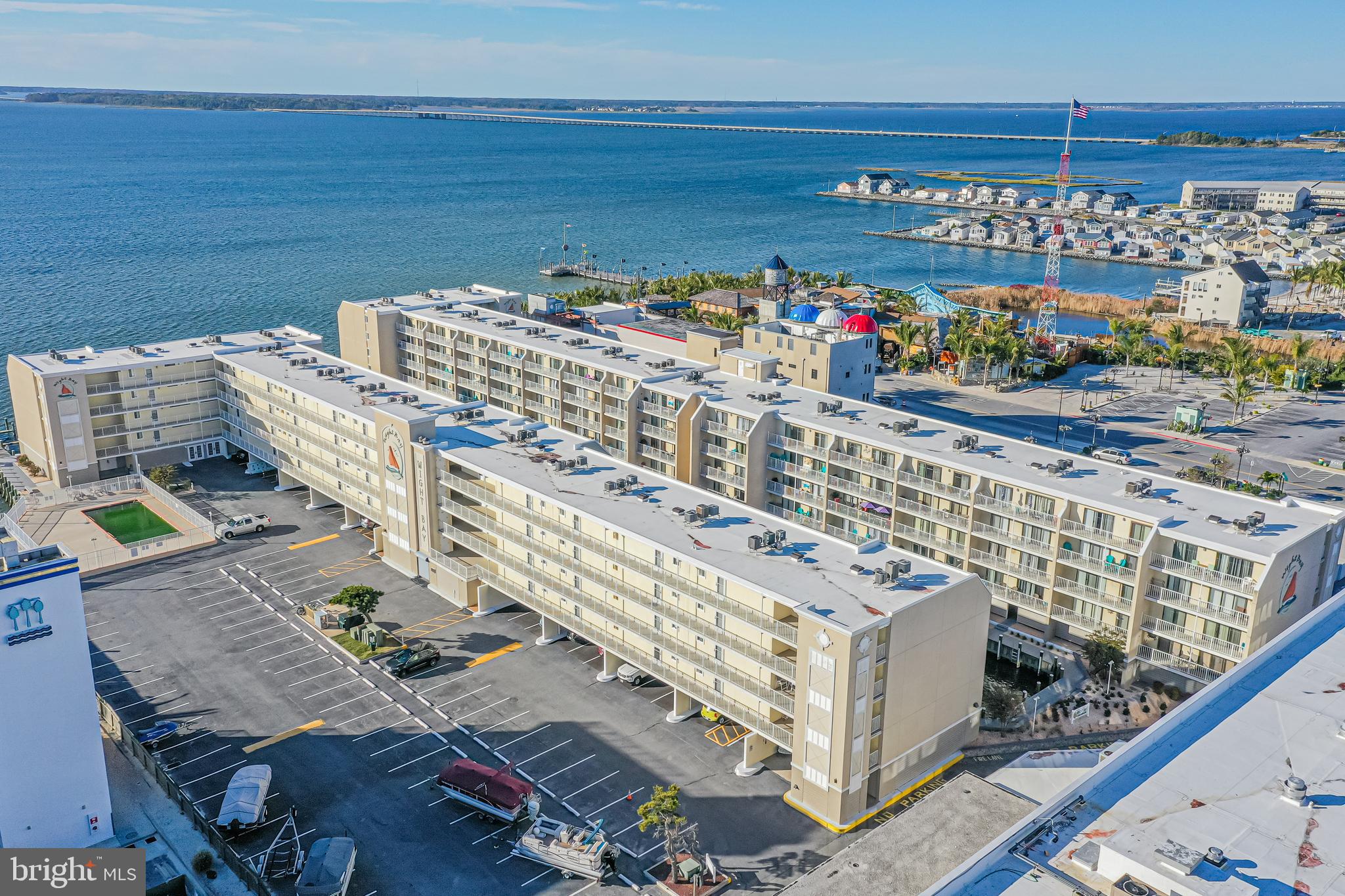 Aerial view of Wight Bay condominium beside blue water, with rows of balconies and a parking lot.