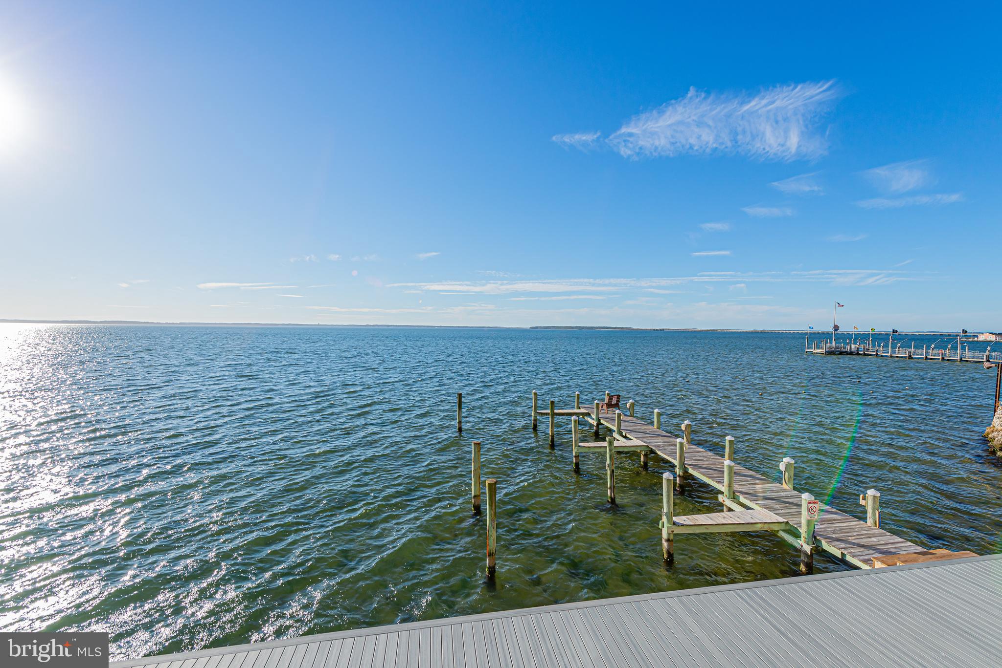 Bay waterfront with a wooden dock extending over the water beneath a bright blue sky.